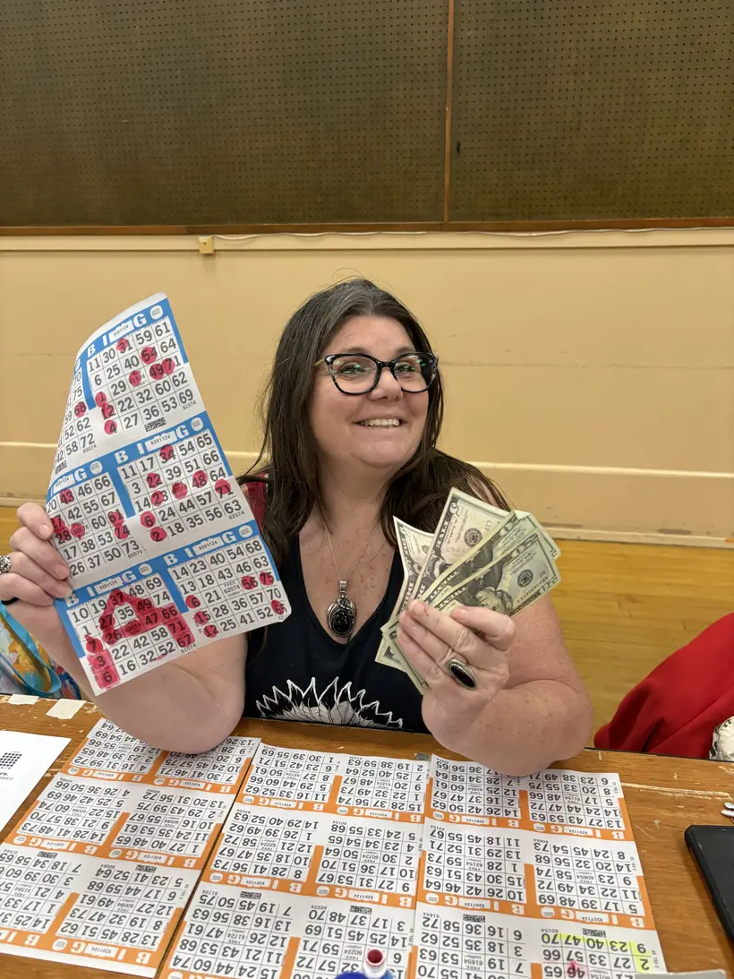 A smiling Wine Country Bingo winner holding cards and cash.