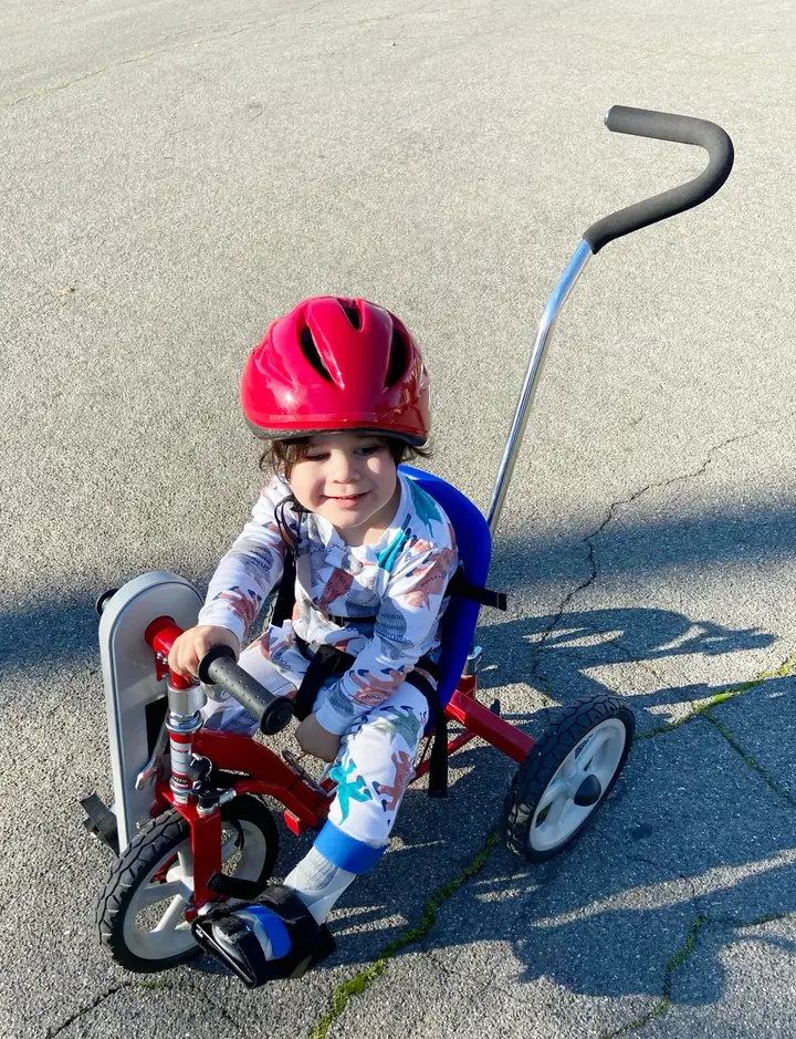 Lukas riding his first red adaptive Tryke outdoors.