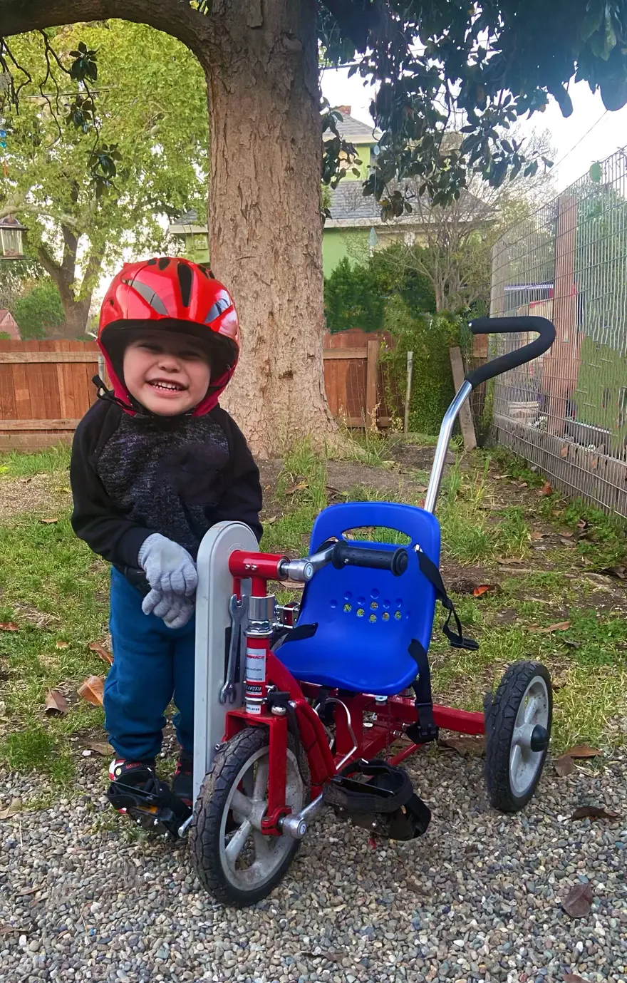 An older Lukas standing beside the red adaptive Tryke he grew with.